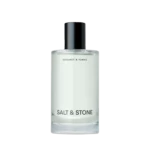 Close-up of a glass perfume bottle with a black spray cap; label reads Salt & Stone, Bergamot & Hinoki visible beneath.