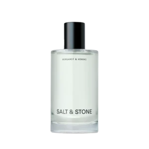 Close-up of a glass perfume bottle with a black spray cap; label reads Salt & Stone, Bergamot & Hinoki visible beneath.