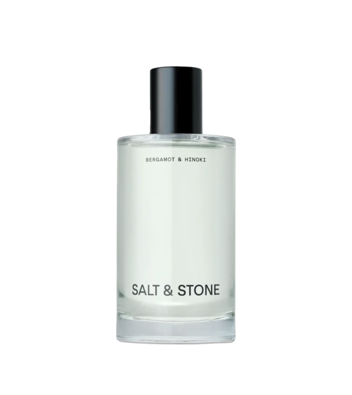 Close-up of a glass perfume bottle with a black spray cap; label reads Salt & Stone, Bergamot & Hinoki visible beneath.