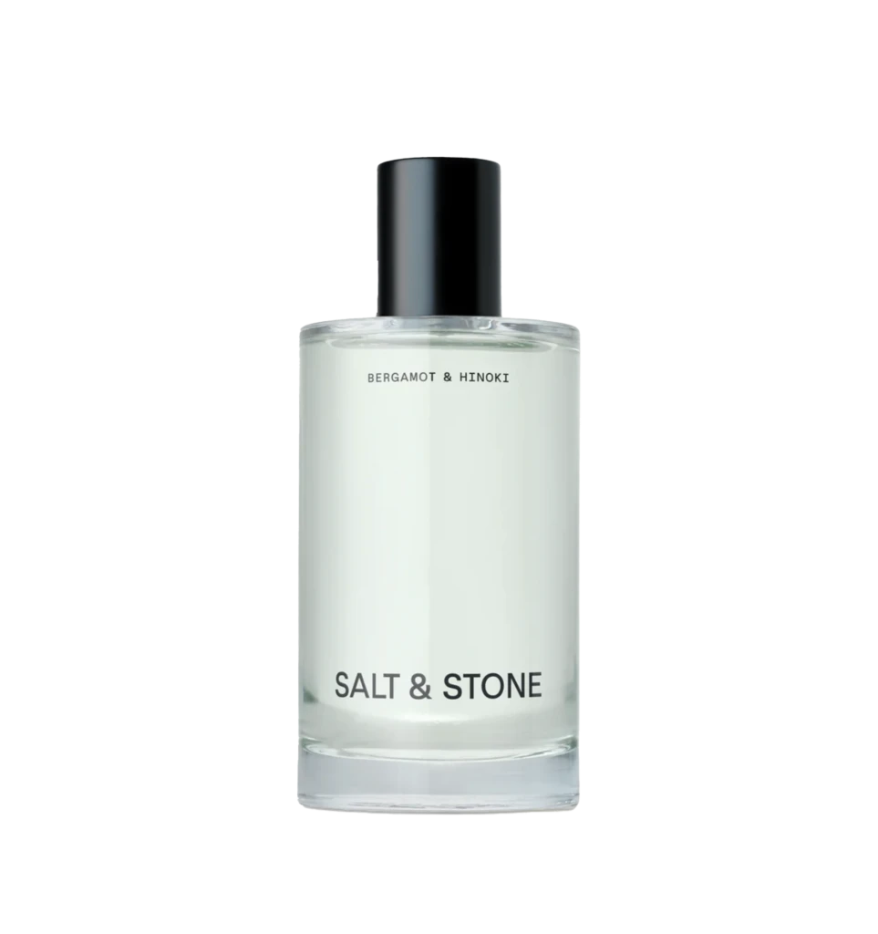 Close-up of a glass perfume bottle with a black spray cap; label reads Salt & Stone, Bergamot & Hinoki visible beneath.