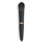 Close-up of a black makeup brush with dense bristles and a copper ferrule against a white background