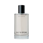 Clear glass bottle with a black cap and the label 'SALT & STONE' visible on a light background, product cosmetics bottle detail
