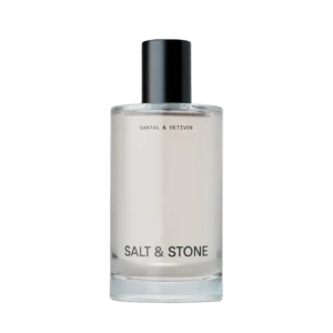 Clear glass bottle with a black cap and the label 'SALT & STONE' visible on a light background, product cosmetics bottle detail