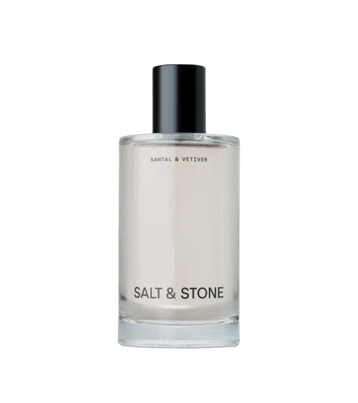 Clear glass bottle with a black cap and the label 'SALT & STONE' visible on a light background, product cosmetics bottle detail