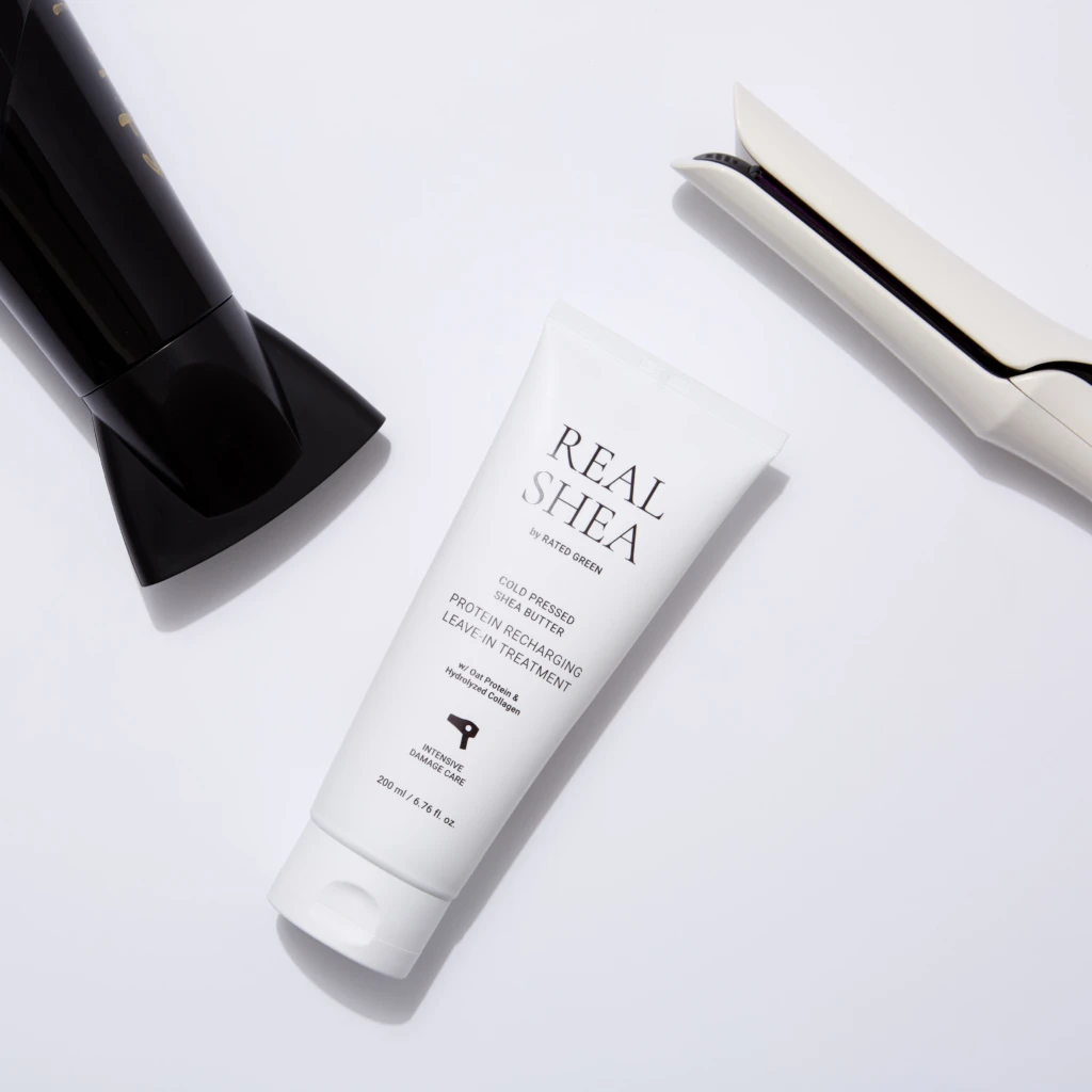 Hair styling tools arranged on a white surface: a black bottle on the left, a white flat iron on the right, and a white tube between them.
