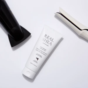 Hair styling tools arranged on a white surface: a black bottle on the left, a white flat iron on the right, and a white tube between them.