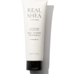 White skincare tube labeled REAL SHEA with 'Cold Pressed Shea Butter' and 'Real Change Treatment' on a black background. Avocado oil listed; 240 ml capacity.
