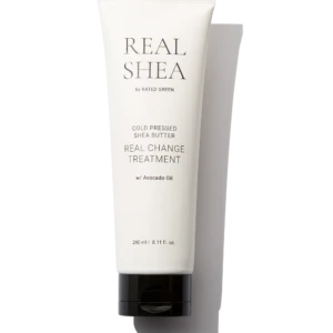 White skincare tube labeled REAL SHEA with 'Cold Pressed Shea Butter' and 'Real Change Treatment' on a black background. Avocado oil listed; 240 ml capacity.