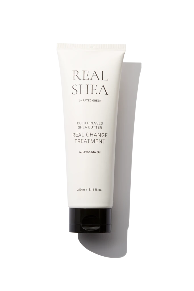 White skincare tube labeled REAL SHEA with 'Cold Pressed Shea Butter' and 'Real Change Treatment' on a black background. Avocado oil listed; 240 ml capacity.