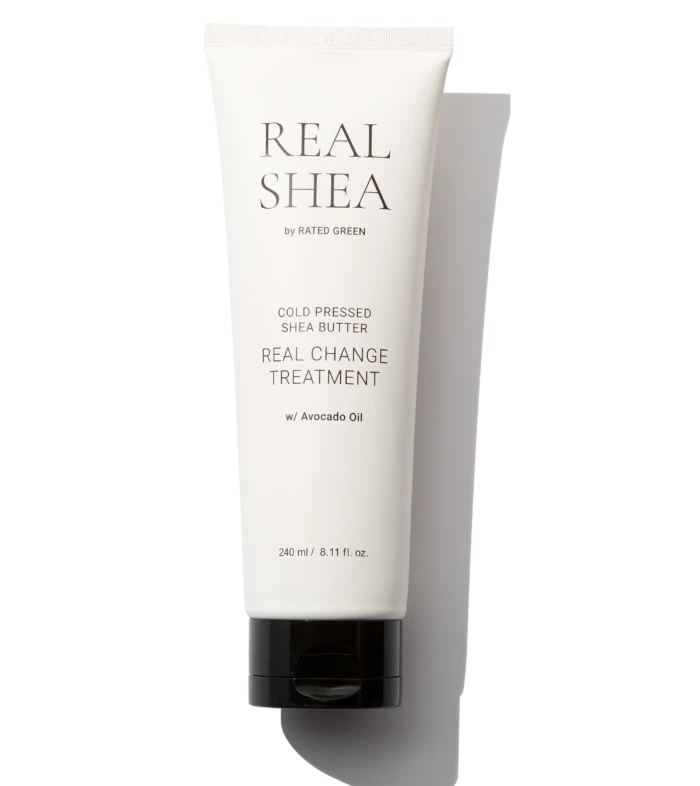 White skincare tube labeled REAL SHEA with 'Cold Pressed Shea Butter' and 'Real Change Treatment' on a black background. Avocado oil listed; 240 ml capacity.