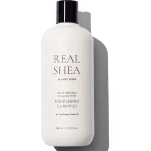 White shampoo bottle with a dark cap, labeled REAL SHEA by Rated Green, against a black background.
