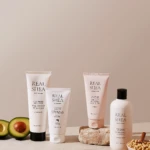 Assorted Real Shea skincare tubes and bottles arranged on a beige surface with avocado halves and chickpeas in a still-life setup.