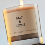Close-up of a lit candle in a glass jar with a minimalist Salt & Stone label.