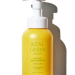 Yellow pump bottle of natural kids shampoo with white pump top against a black background; label reads 'Real Green' and 'Natural Kids Shampoo'.