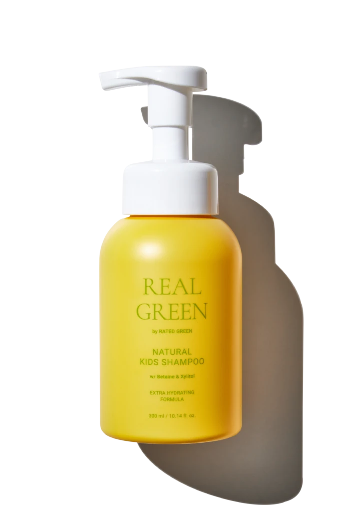 Yellow pump bottle of natural kids shampoo with white pump top against a black background; label reads 'Real Green' and 'Natural Kids Shampoo'.