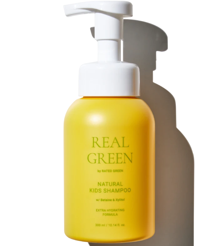 Yellow pump bottle of natural kids shampoo with white pump top against a black background; label reads 'Real Green' and 'Natural Kids Shampoo'.