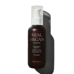 Brown glass bottle with white pump labeled 'REAL ARGAN' containing smoothing hair serum, 150 ml, against a dark background.