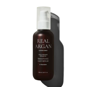Brown glass bottle with white pump labeled 'REAL ARGAN' containing smoothing hair serum, 150 ml, against a dark background.