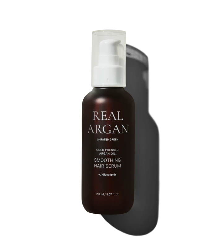 Brown glass bottle with white pump labeled 'REAL ARGAN' containing smoothing hair serum, 150 ml, against a dark background.