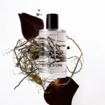Perfume bottle labeled Black Rose & Oud surrounded by dried red rose petals and twigs on a white background