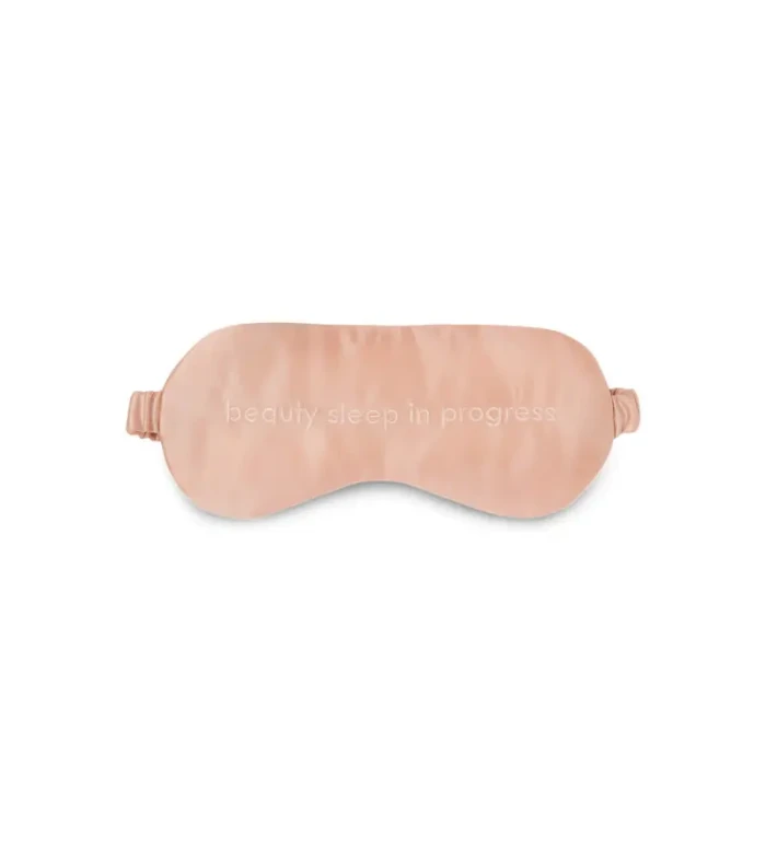 Pink satin sleep mask with adjustable straps and embroidered slogan 'beauty sleep in progress'.