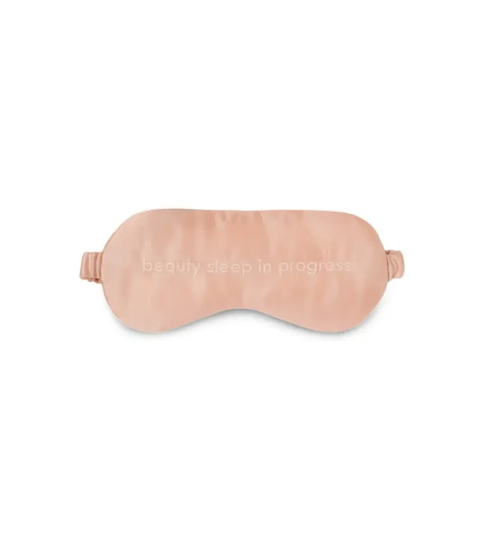 Pink satin sleep mask with adjustable straps and embroidered slogan 'beauty sleep in progress'.