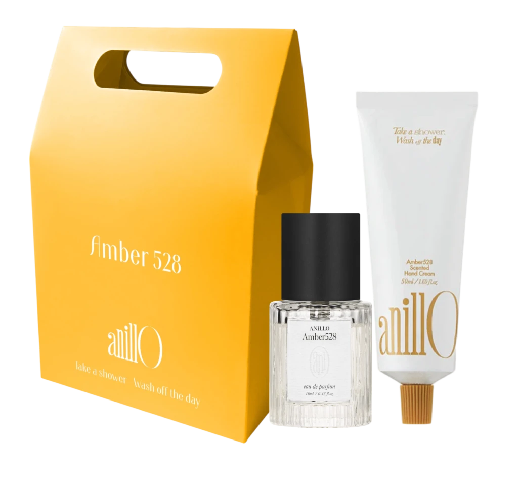 Bright yellow gift-box style package with a built-in handle, accompanied by a clear glass fragrance bottle labeled Amber528 and white boxed packaging nearby.