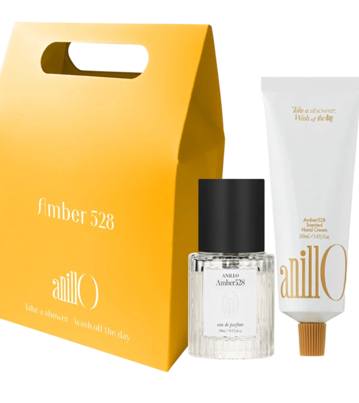 Bright yellow gift-box style package with a built-in handle, accompanied by a clear glass fragrance bottle labeled Amber528 and white boxed packaging nearby.