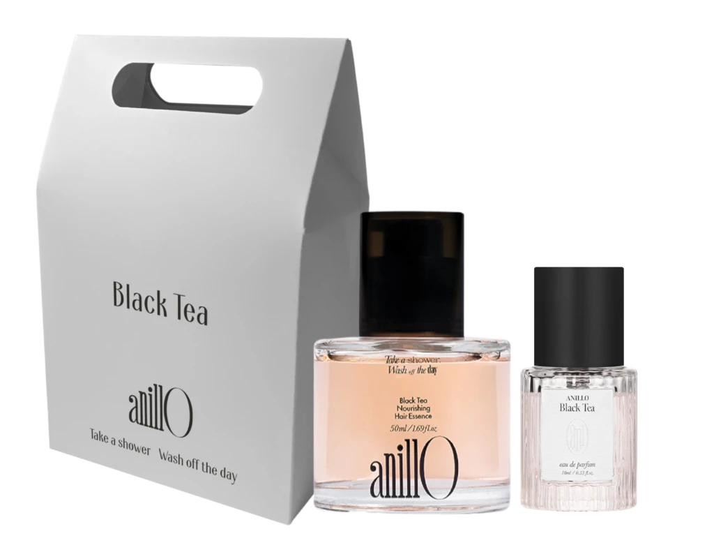 Tall white packaging box with a built-in handle reading 'Black Tea' beside a pink perfume bottle and a clear glass bottle on a dark background; product set.