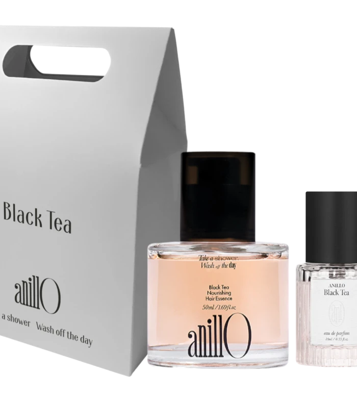 Tall white packaging box with a built-in handle reading 'Black Tea' beside a pink perfume bottle and a clear glass bottle on a dark background; product set.