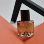 Clear glass perfume bottle with amber liquid and a dark cap resting on a peach-colored surface.