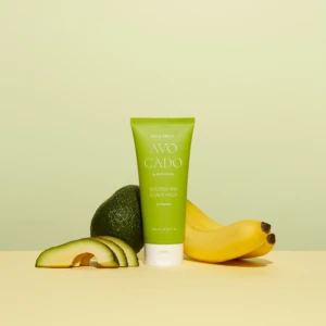 Green tube of Avocado Nourishing Scalp Pack with avocado halves and bananas surrounding it against a pale yellow backdrop