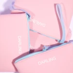 Close-up of a pink backpack with light blue zippers and lavender straps; partial text 'DARLING' visible.