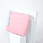 Pink zippered pouch with a light blue zipper resting on white stepped blocks against a pale background.