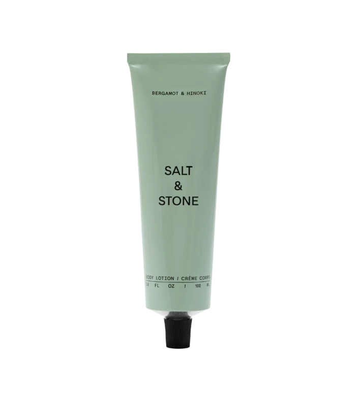 Pale green Bergamot & Hinoki body lotion tube with a black cap on a black background, upright and centered.