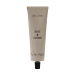 Beige squeeze tube labeled 'SALT & STONE' with a black cap, standing upright with 'Body Lotion' text at the bottom against a black background.