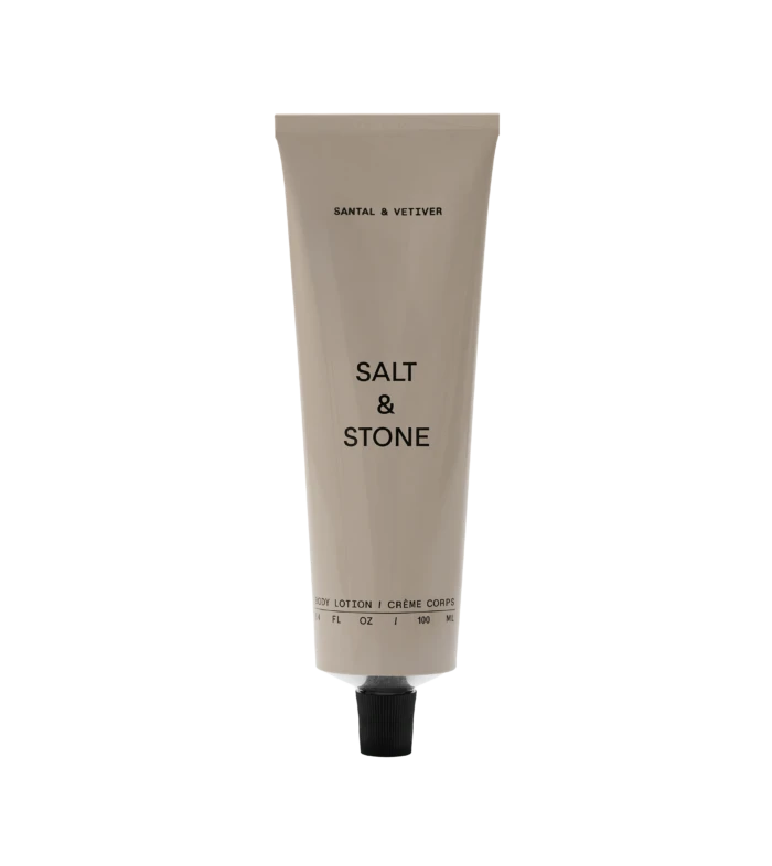 Beige squeeze tube labeled 'SALT & STONE' with a black cap, standing upright with 'Body Lotion' text at the bottom against a black background.