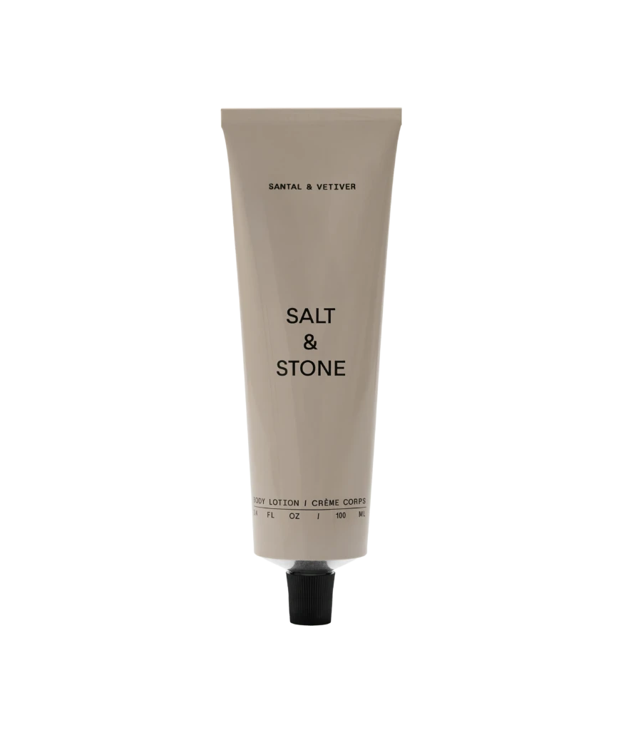 Beige squeeze tube labeled 'SALT & STONE' with a black cap, standing upright with 'Body Lotion' text at the bottom against a black background.