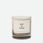 Clear glass candle jar with white label reading 'SALT & STONE' against a pale backdrop.