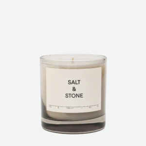 Clear glass candle jar with white label reading 'SALT & STONE' against a pale backdrop.