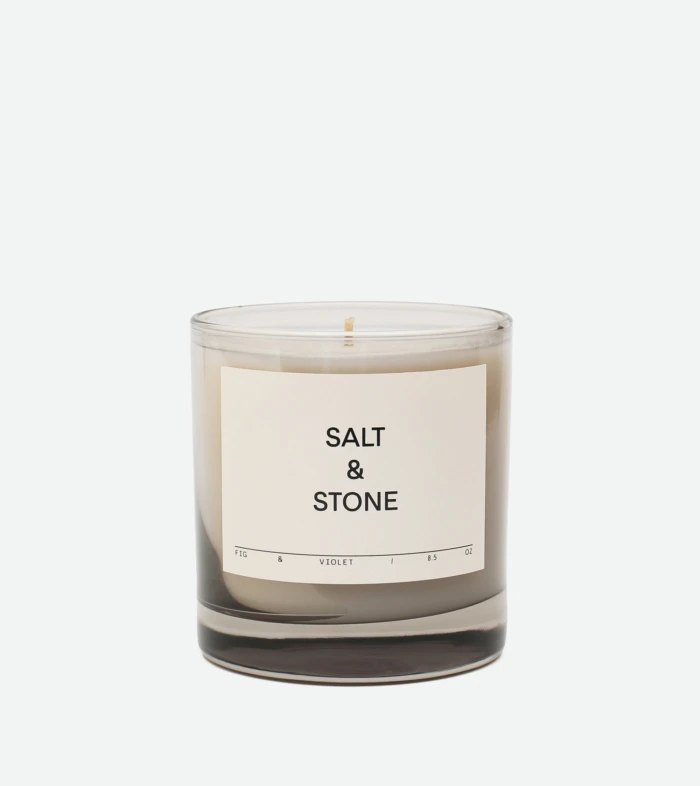 Clear glass candle jar with white label reading 'SALT & STONE' against a pale backdrop.
