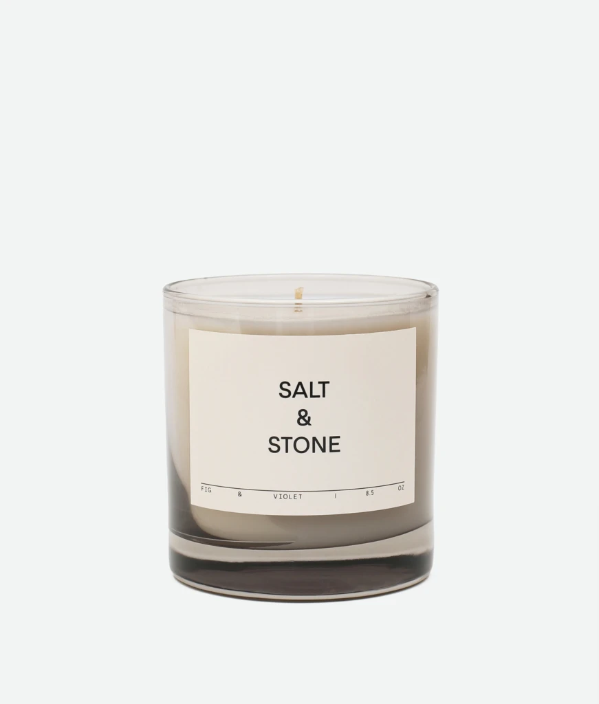 Clear glass candle jar with white label reading 'SALT & STONE' against a pale backdrop.