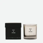 Salt & Stone scented candle in a frosted glass jar beside its black box, product packaging visible on a white background, close-up shot