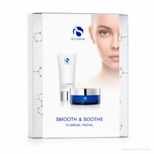 Boxed iS Clinical skincare set (Smooth & Soothe Clinical Facial) with a white tube and blue jar in front of a partial model's face on a white background.