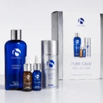 Blue IS CLINICAL Cleansing Complex bottle with smaller serum bottles and a silver container beside a Pure Calm Collection box.
