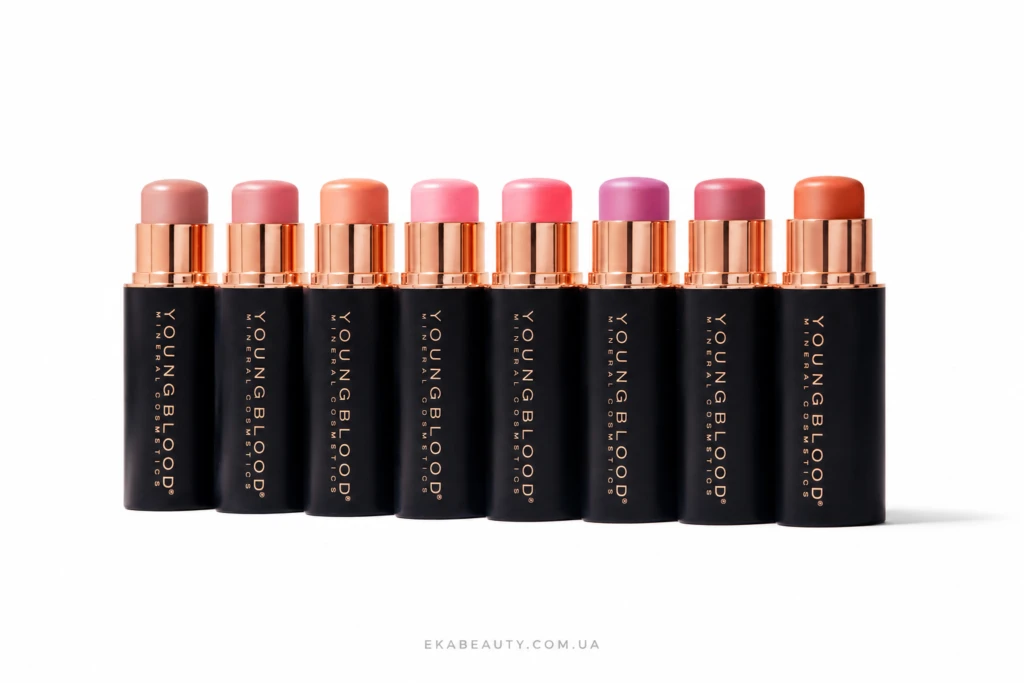 Row of black lipstick tubes with rose-gold caps in a line, showing pink to coral lipstick shades on a white background.