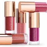 Assorted Youngblood mineral lip glosses with rose-gold caps arranged on a white background.