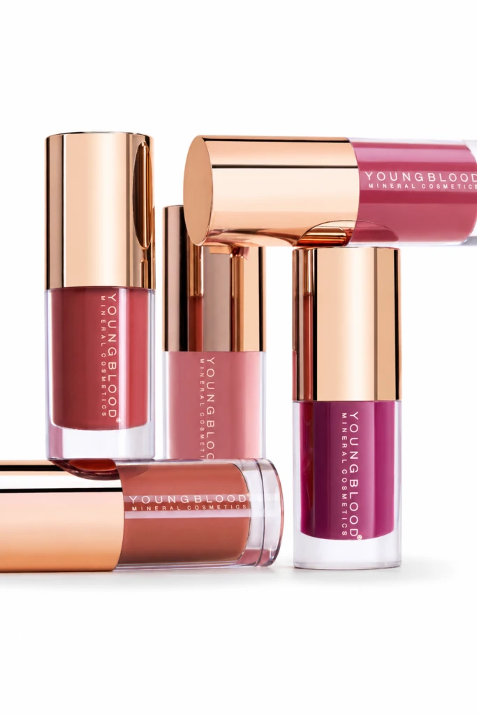 Assorted Youngblood mineral lip glosses with rose-gold caps arranged on a white background.