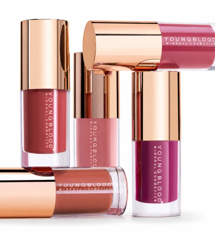 Assorted Youngblood mineral lip glosses with rose-gold caps arranged on a white background.