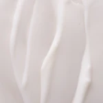 Close-up of a smooth, white abstract sculpture with ribbon-like curves against a pale pink background, emphasizing form over detail.